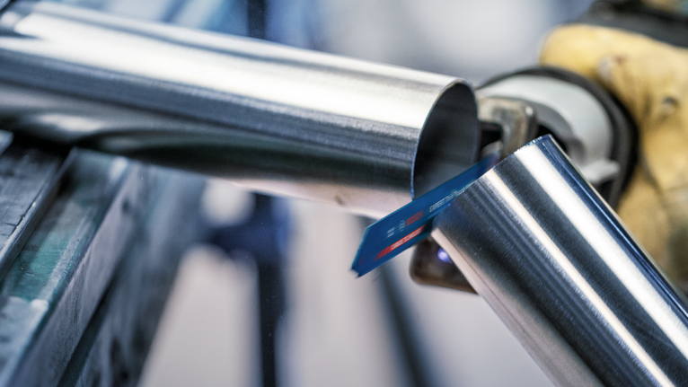 안전 장비를 착용한 사람이 왕복톱으로 금속 파이프를 자르고 있습니다.