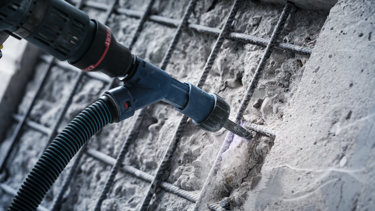 노출된 철근 근처의 콘크리트를 로터리 해머로 드릴링하는 중 발생하는 먼지를 제거하는 모습.