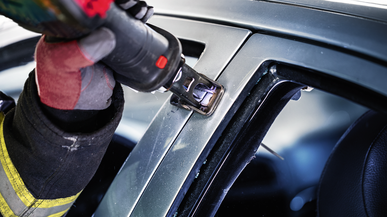 안전 장비를 착용한 사람이 전동 공구를 사용하여 자동차 프레임을 절단하고 있습니다.