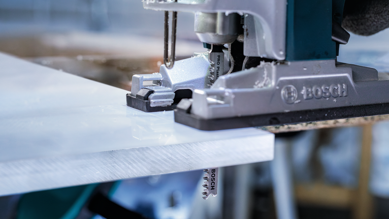 작업장에서 직소톱으로 흰색 플라스틱 시트를 자르고 있는 모습.