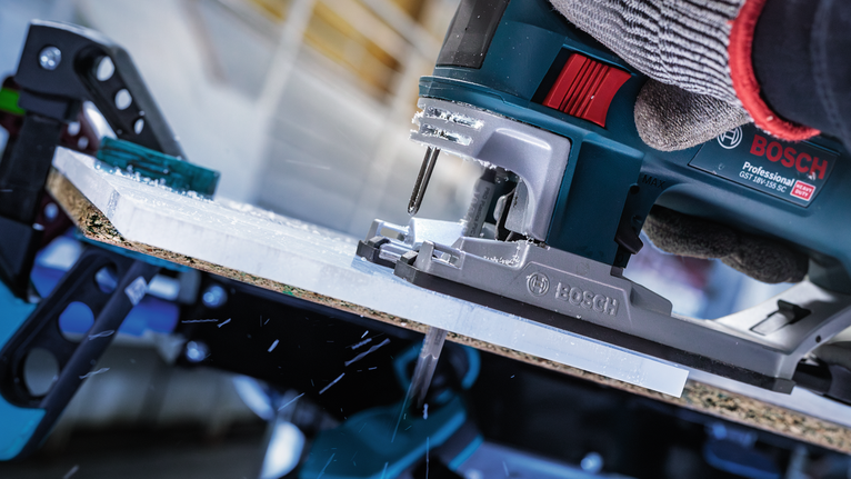 안전 장비를 착용한 사람이 직소톱을 사용하여 재료판을 자르고 있습니다.