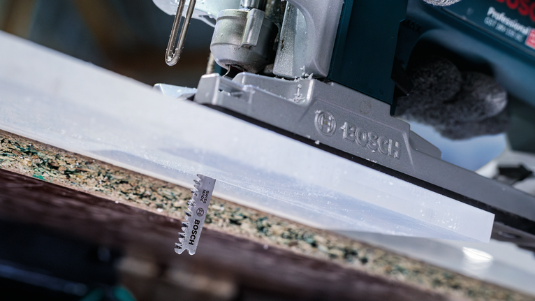 안전 장비를 착용한 사람이 직소톱으로 합판을 자르고 있습니다.