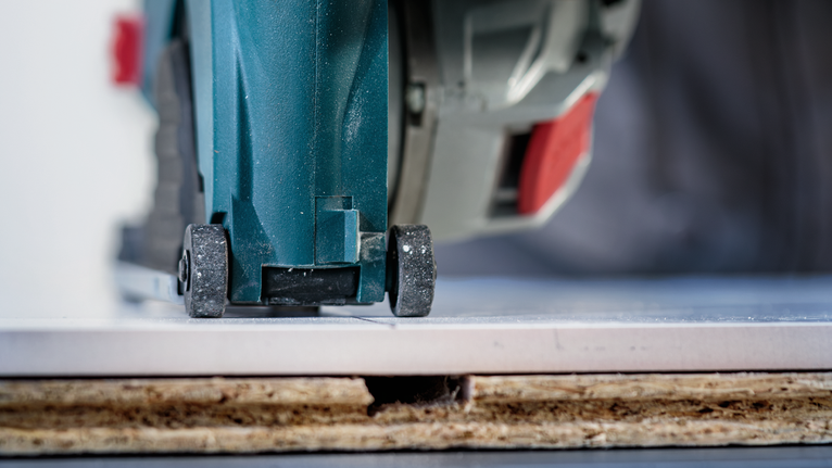 원형톱으로 나무 표면에 부착된 타일을 자르고 있다.