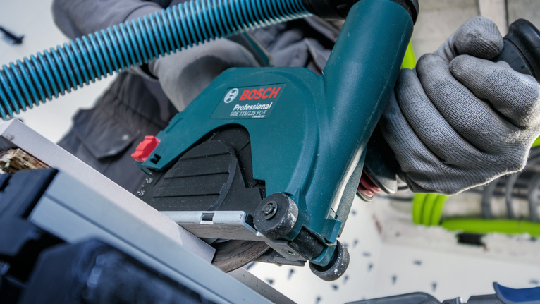 안전 장비를 착용한 사람이 원형 톱으로 재료를 자르고 있습니다.