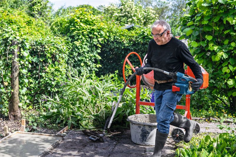 안전 장비를 착용한 사람이 전동 공구를 사용하여 야외에서 콘크리트를 섞고 있습니다.