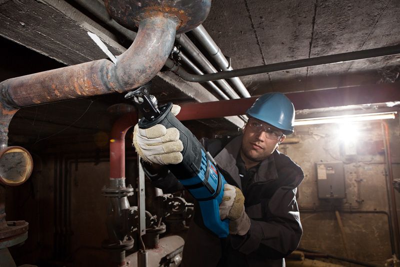 안전장비를 착용한 사람이 왕복톱으로 금속 파이프를 자릅니다.