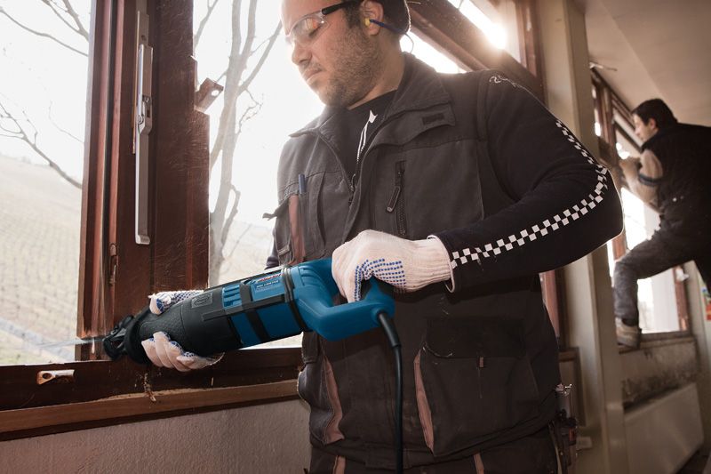 안전 장비를 착용한 사람이 왕복톱을 사용해 창틀을 자릅니다.