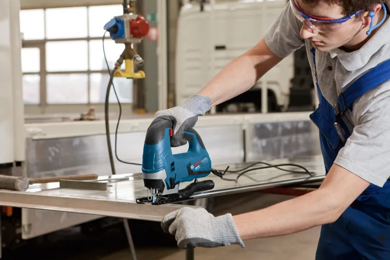 안전장비를 착용한 사람이 퍼즐을 사용해 금속판을 자릅니다.