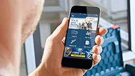 손에 스마트폰을 들고 있는 사람, 앱 화면이 보임, 배경은 작업 공간.