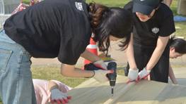 두 명의 작업자가 나무에 전동 드릴로 작업하고 있다.