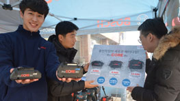 두 남성이 Bosch 배터리를 들고, 한 남성이 포스터를 보고 있다.